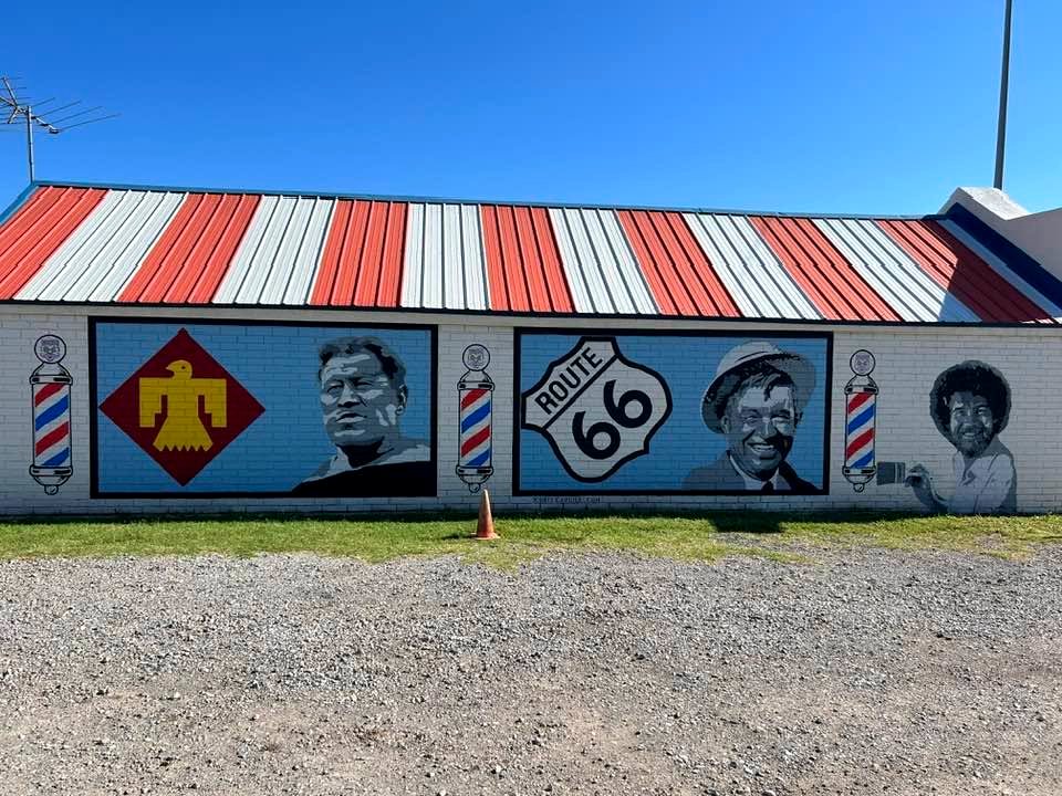 Route 66 mural painted on the side of Doc's Barber Shop, with barber poles and the striped metal roof