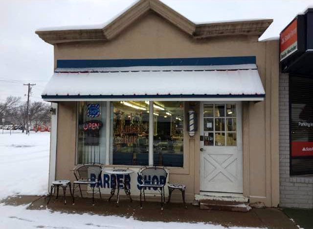 Doc's Barber Shop storefront in the snow with the OPEN sign lit and a barber pole in the window